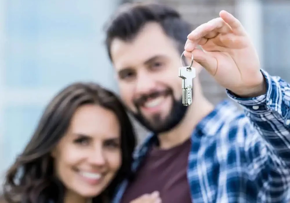 Pareja de hombre y mujer, quienes sonríen mientras muestran las llaves de su casa