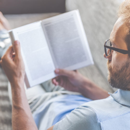 Hombre descalzo y relajado recostado sobre un sillón, leyendo.