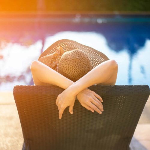 mujer con sombrero disfrutando del sol al lado de una piscina