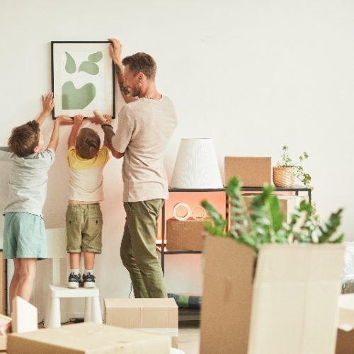 Un papá y dos hijos colocan un cuadro en la pared